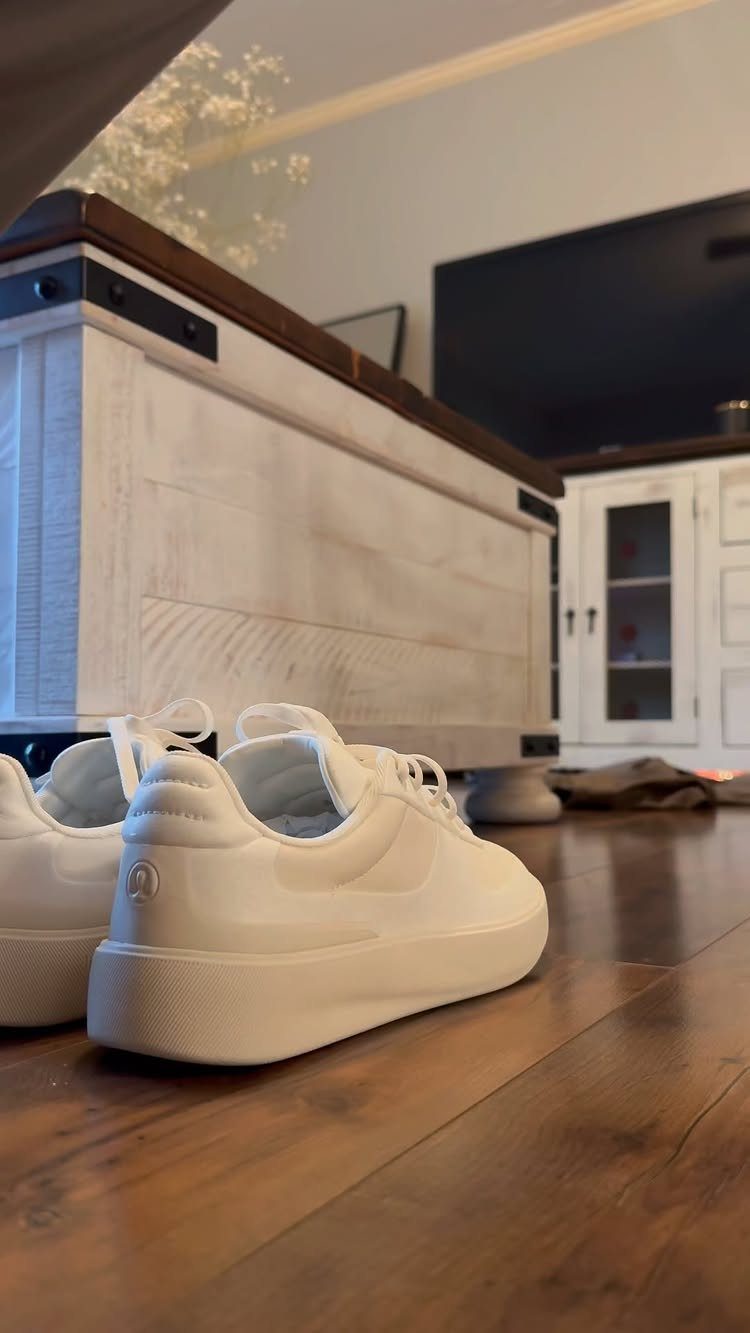 White streamlined sneakers resting on a wooden floor in a living room setting.