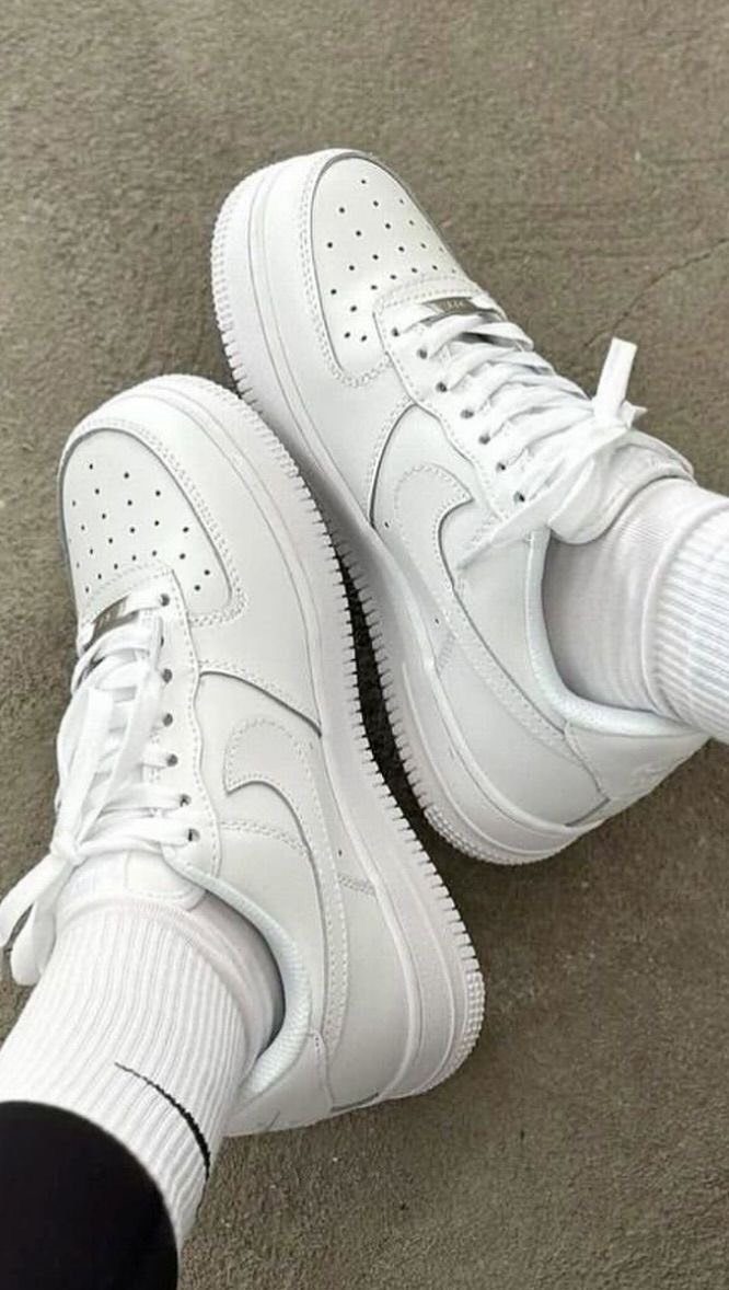 White Nike Air Force 1 sneakers worn with white socks on a concrete ground.