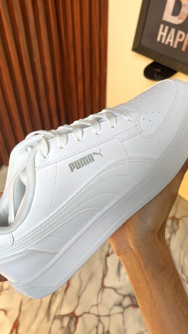 A white Puma sneaker held by a person's hand against a yellow wall.