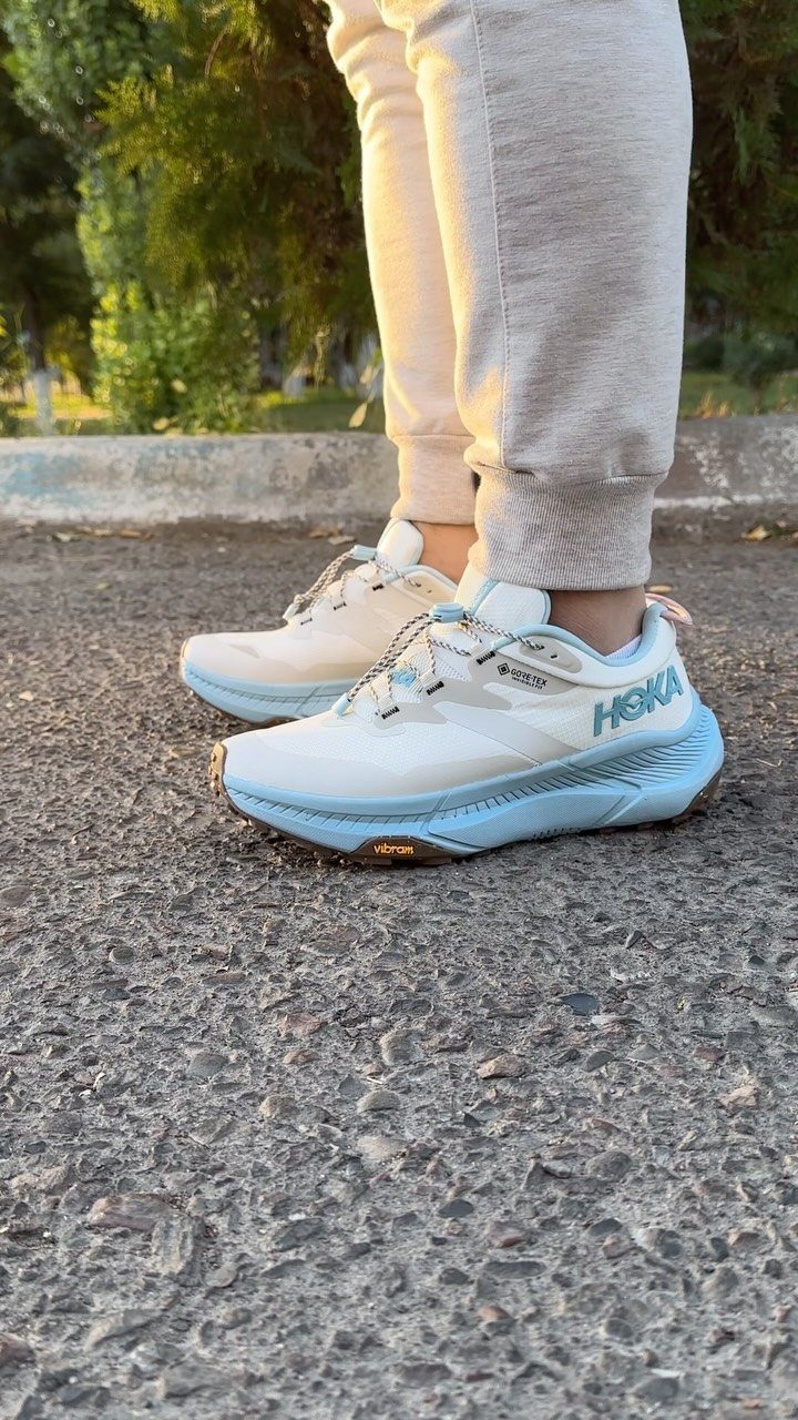 Person wearing light beige sweatpants and white and light blue Hoka running shoes on asphalt.