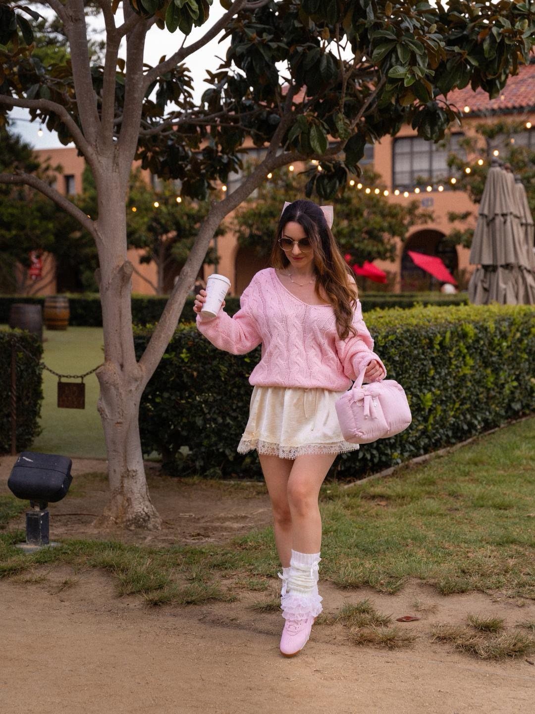 A woman walking in a garden wearing a pink sweater, lace skirt, and pink fuzzy sneakers.