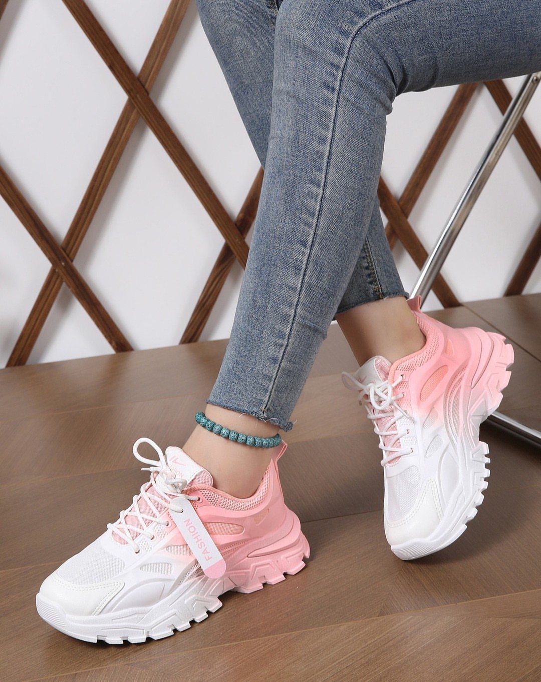 Person wearing pink and white chunky platform sneakers with blue jeans on a wooden floor.