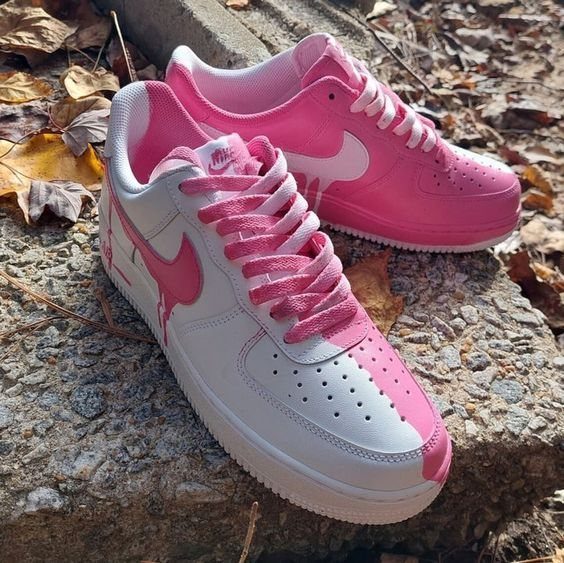 Pink and white Nike Air Force 1 sneakers resting on a stone ledge with autumn leaves.