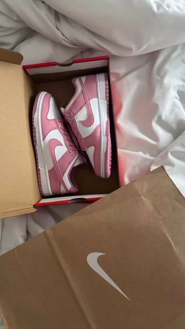 Pink and white Nike Dunk Low sneakers sitting inside an open shoebox on white sheets.