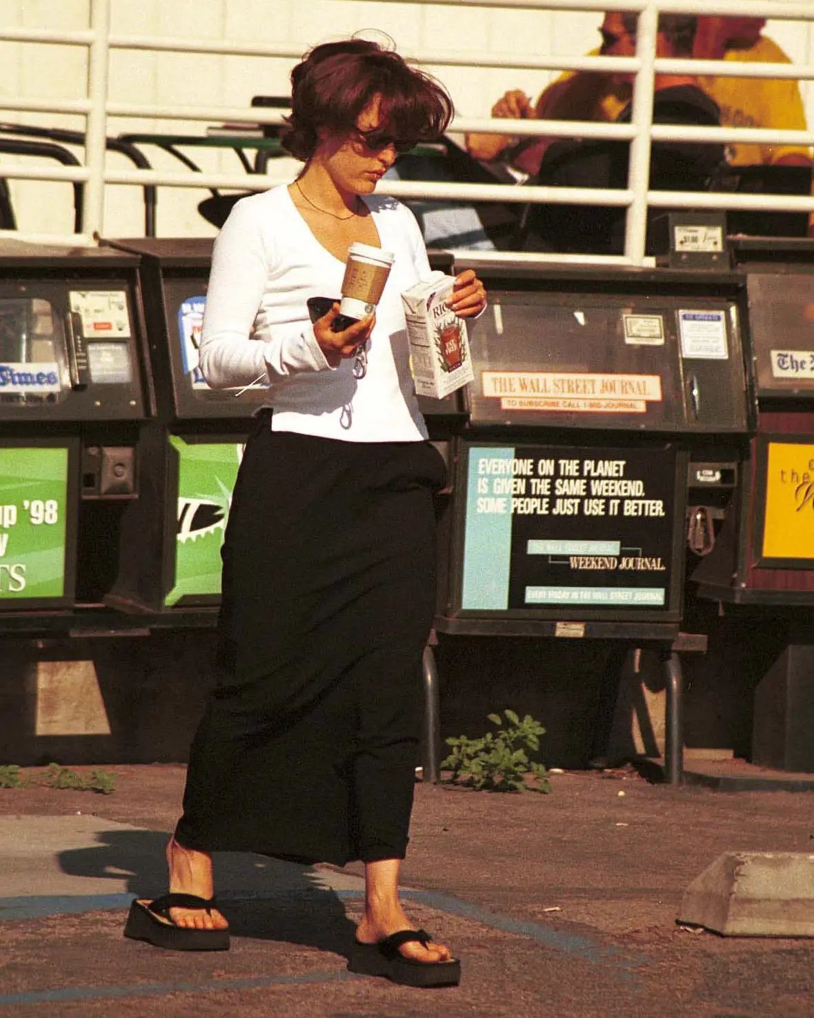 Woman walking in a black skirt and white shirt wearing black platform flip flops.