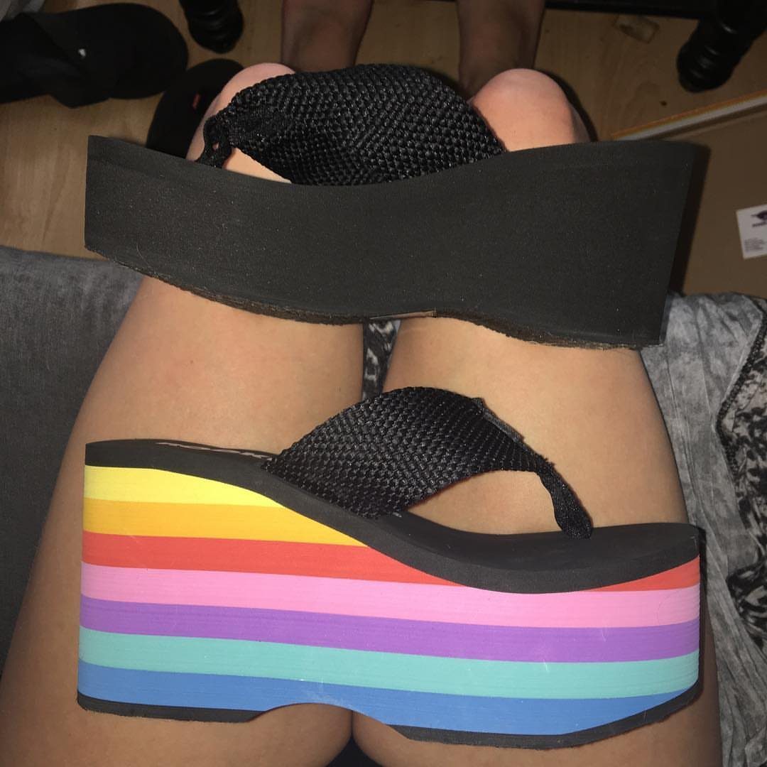 Rainbow striped platform wedge sandals with black straps worn on a person's feet.
