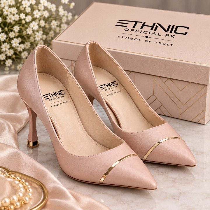 Nude pointed toe high heels with gold trim sitting on a marble surface near a box.