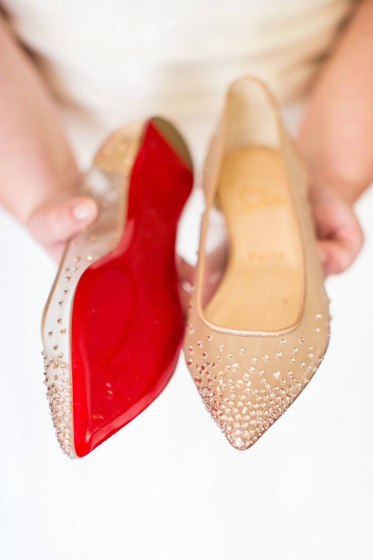 Cream pointed-toe flats with sparkling embellishments and one shoe showing a bright red sole.
