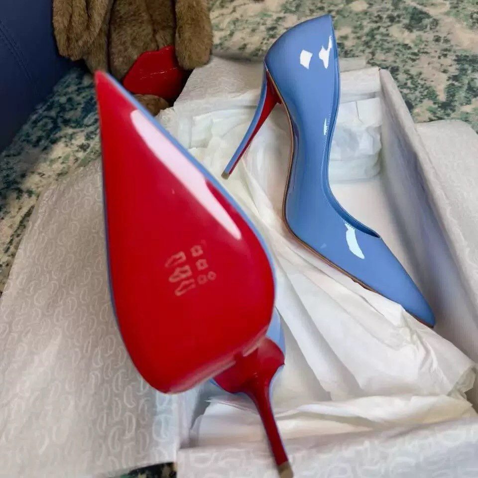 Light blue patent leather stiletto pumps with red soles resting in a white gift box.