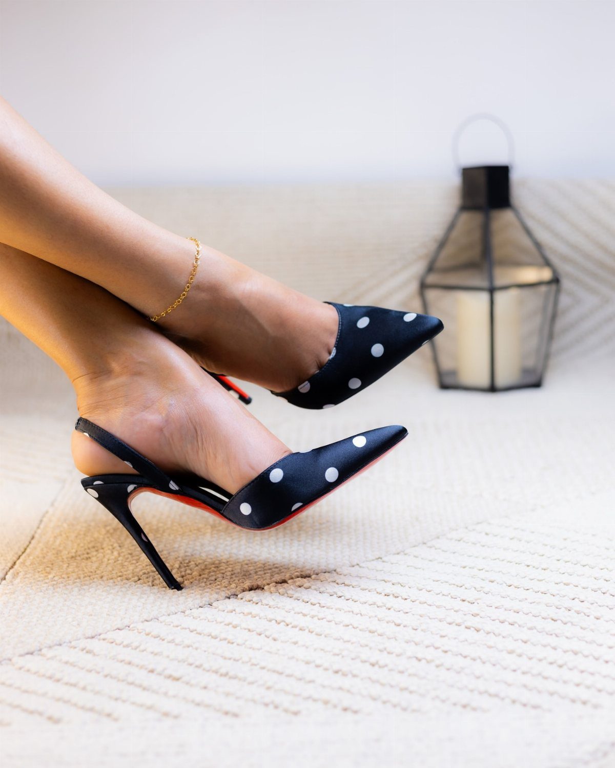 Black polka dot slingback heels with red soles worn on a person's feet.