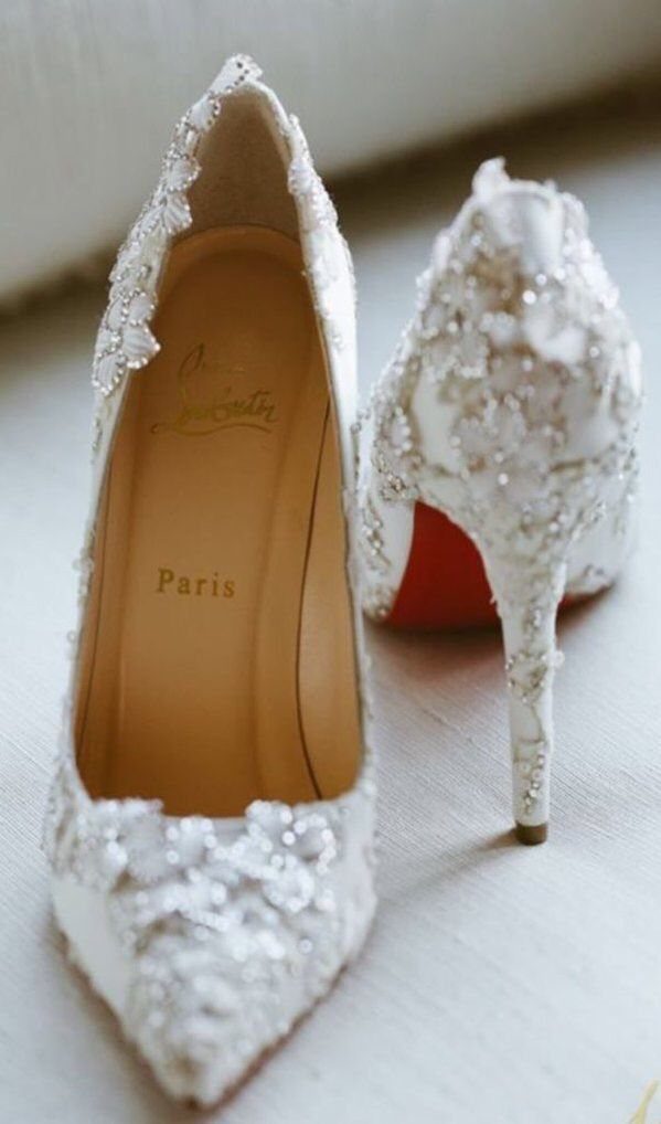 White satin pointed-toe heels featuring elegant floral lace and beadwork decorations on a light surface.