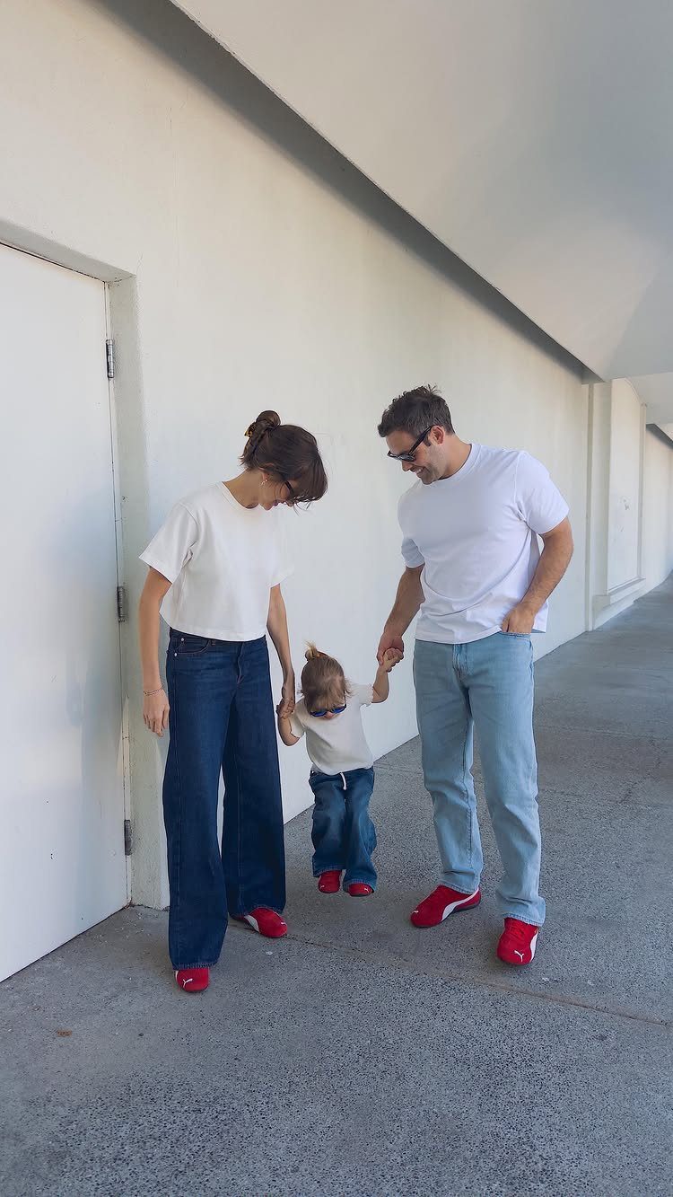 A woman, man, and child walking together wearing white shirts and red sneakers.
