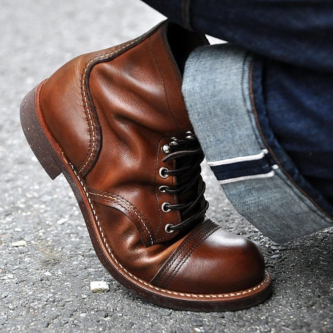 A brown leather lace-up boot with creased leather worn with cuffed denim jeans on asphalt.