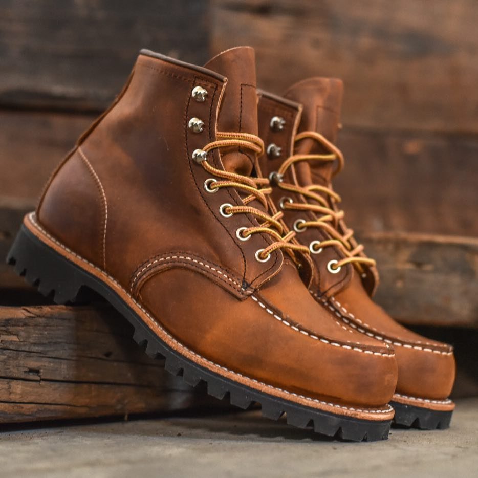 Two brown leather lace-up boots with thick black soles resting on rustic wooden beams.