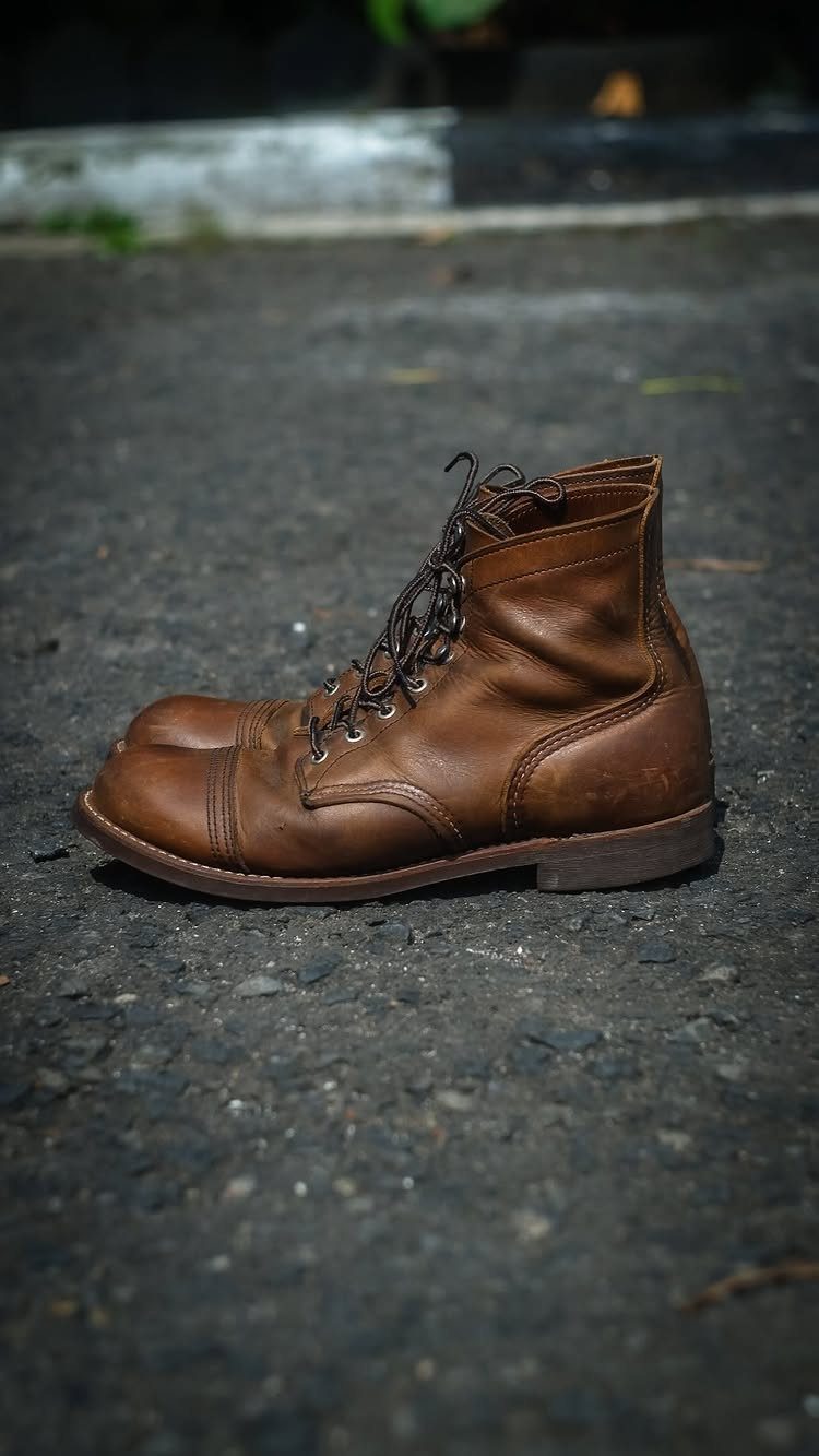 Brown leather Iron Ranger work boots resting on a dark asphalt ground.