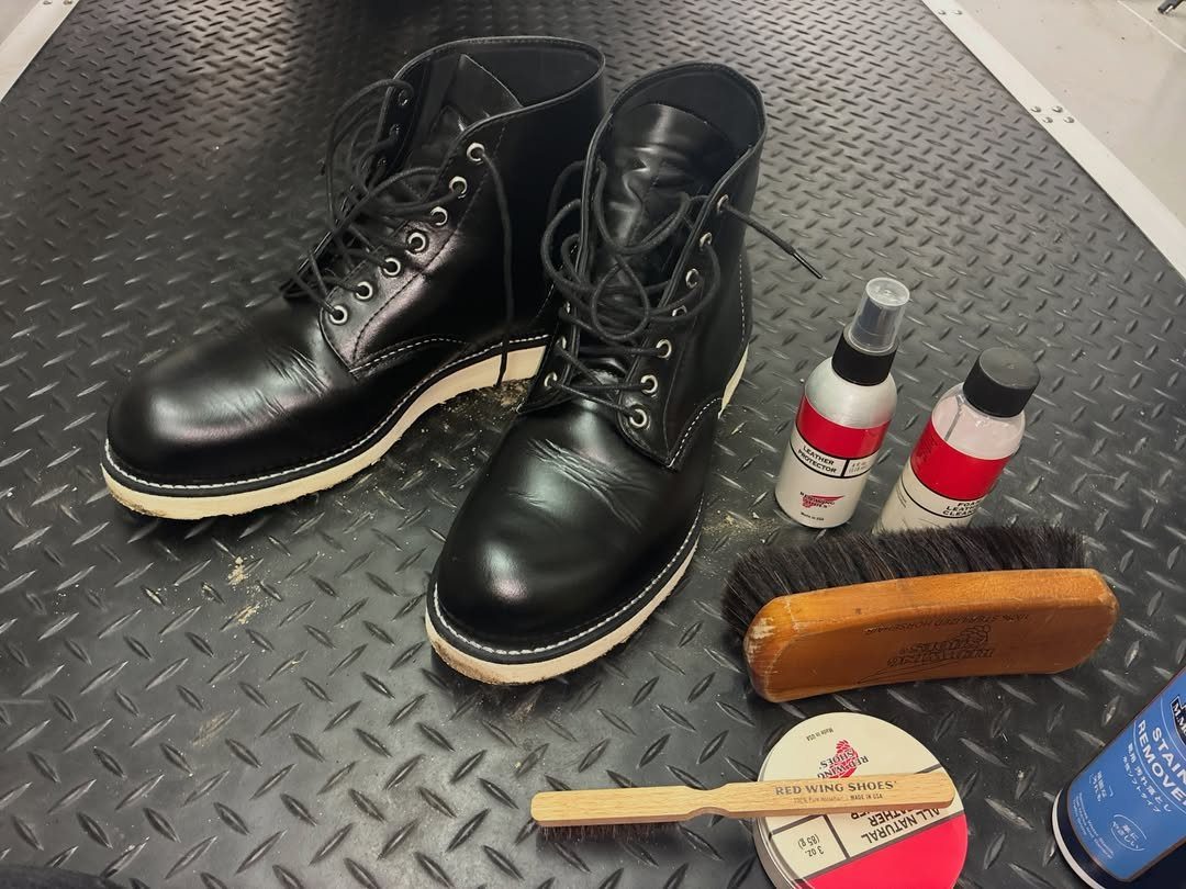 Black leather boots surrounded by various leather cleaning and conditioning products on a metal surface.