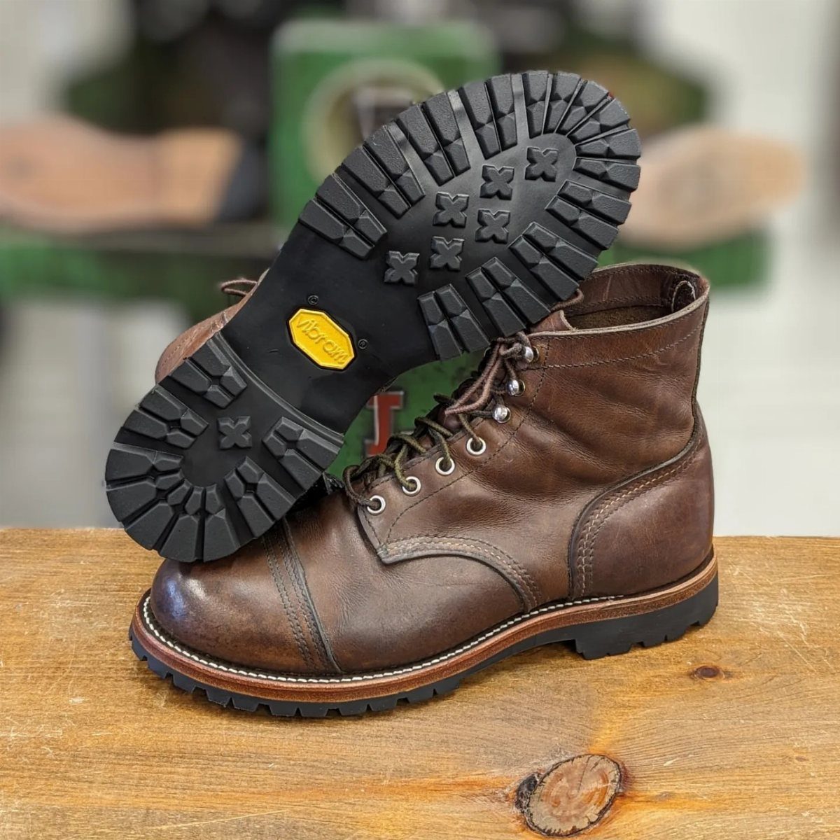 Brown leather boots showing a thick black Vibram lugged sole on a wooden surface.