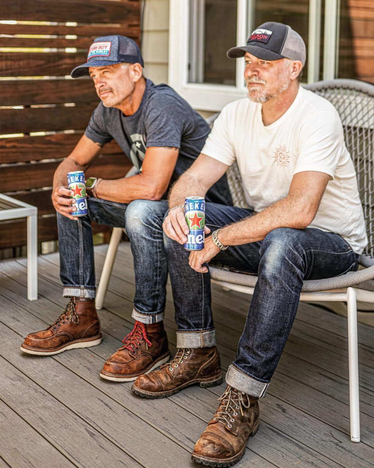 Two men in denim jeans and brown leather boots sitting on a wooden deck.