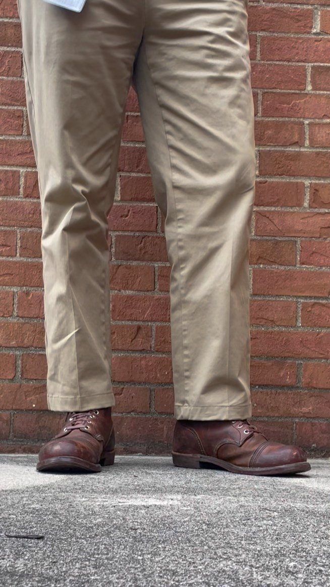 Person wearing tan chinos and brown leather boots standing against a red brick wall.