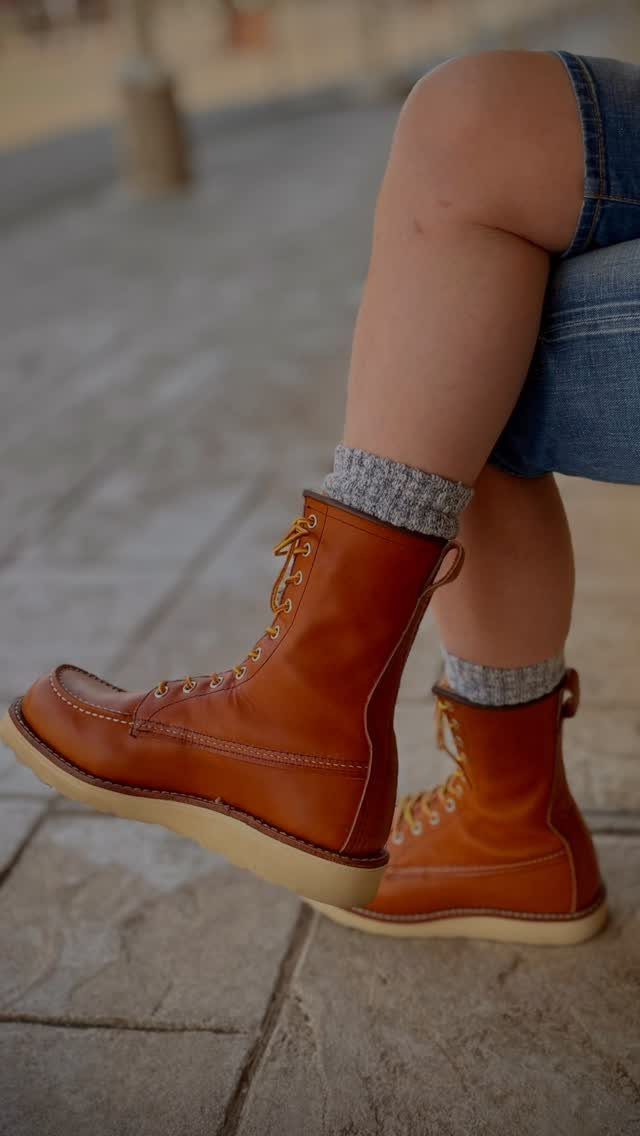 Tan leather boots with grey socks and denim shorts on a person sitting outdoors.
