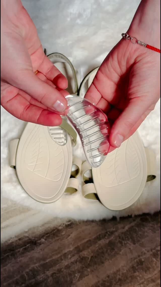 Hands holding a clear gel arch support insole over a pair of beige sandals.
