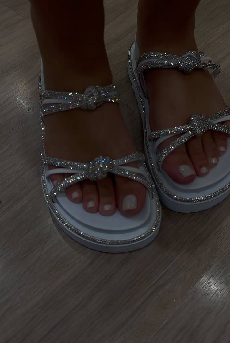 Silver rhinestone-encrusted white platform sandals worn on feet over a wooden floor.