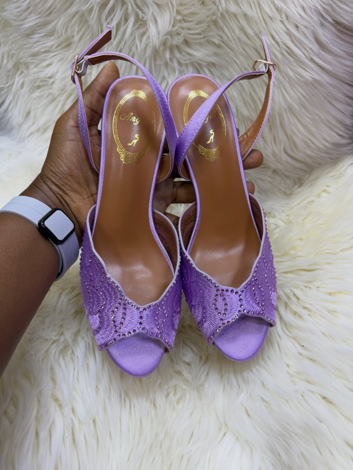 Lavender purple open-toe high-heeled sandals with sparkling details held against white faux fur.