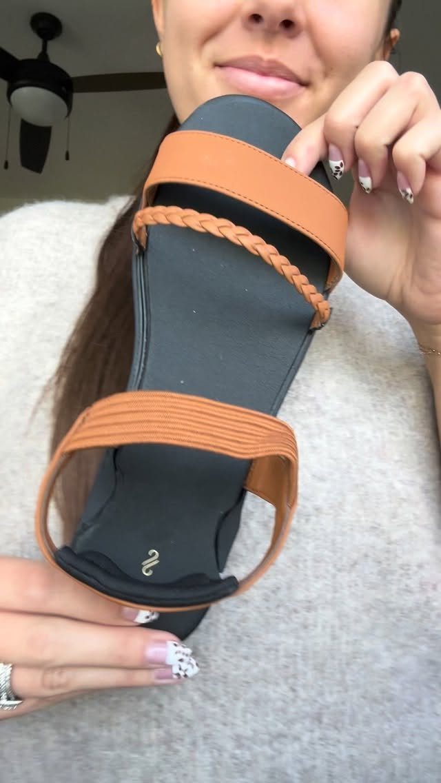 A person holding a tan and black braided sandal with patterned fingernails.