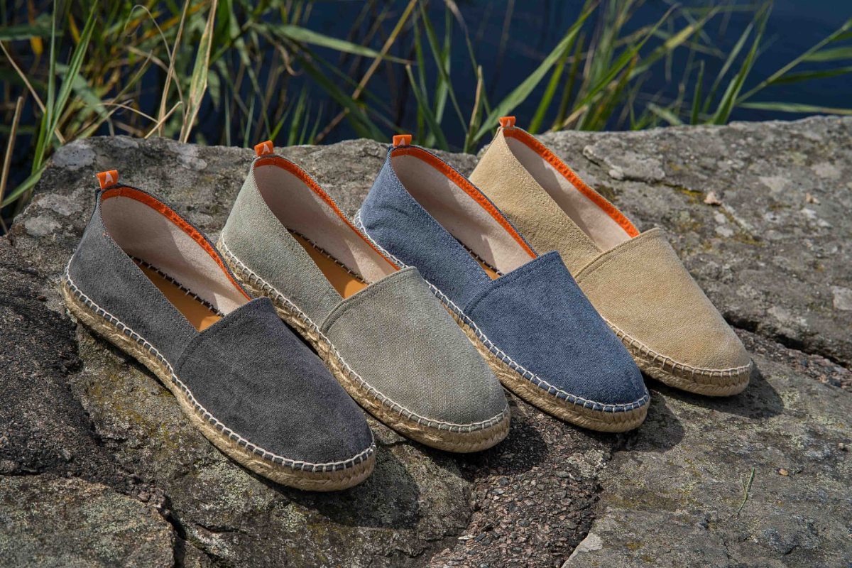 Four pairs of canvas espadrilles in different colors resting on a large rock outdoors.
