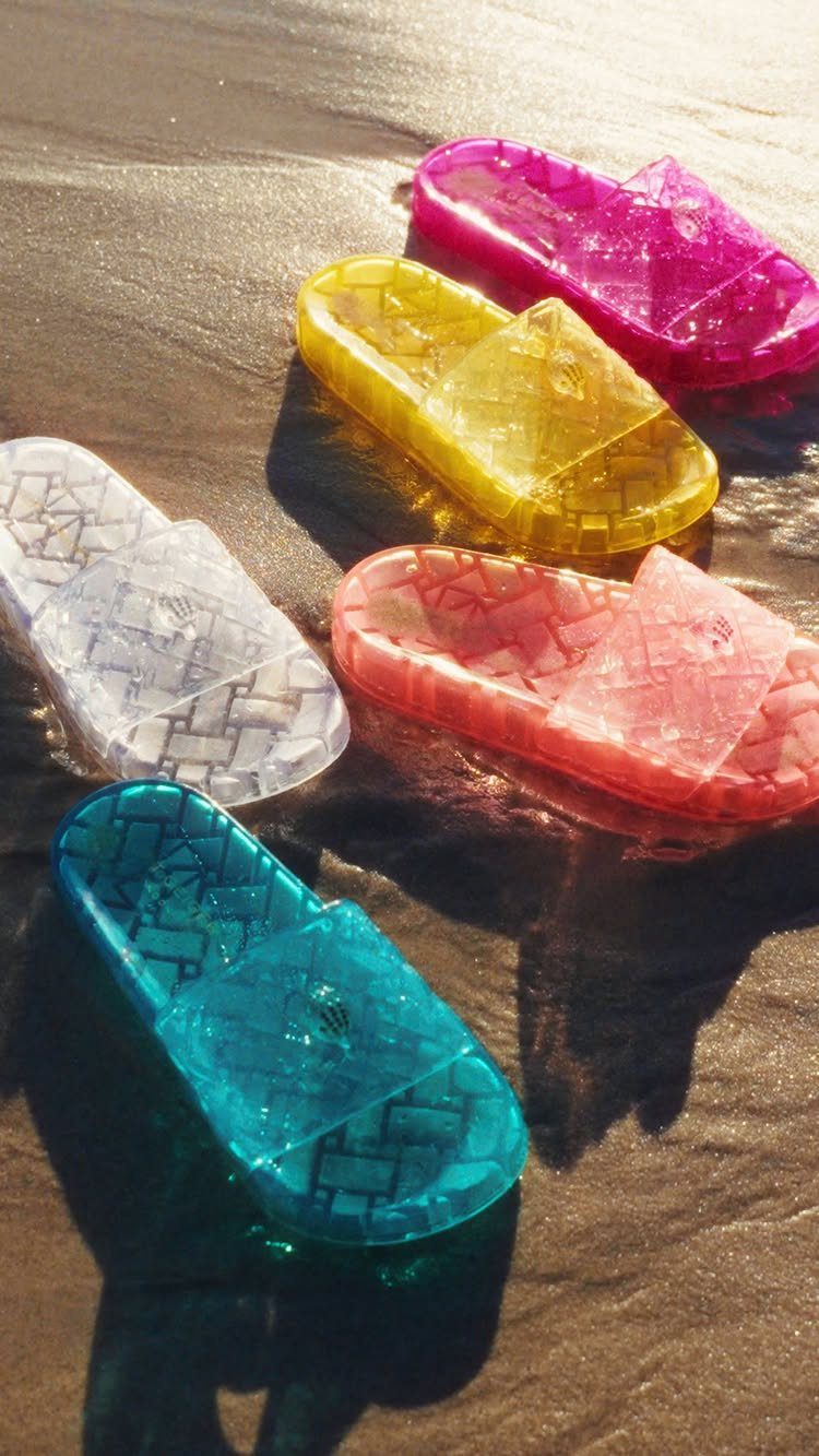 Translucent colorful plastic sliders scattered across wet sand under bright sunlight.