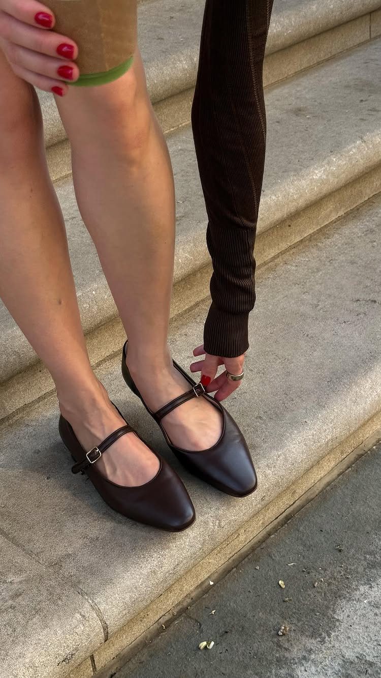 Dark brown leather ballet flats with thin straps worn on stone steps.