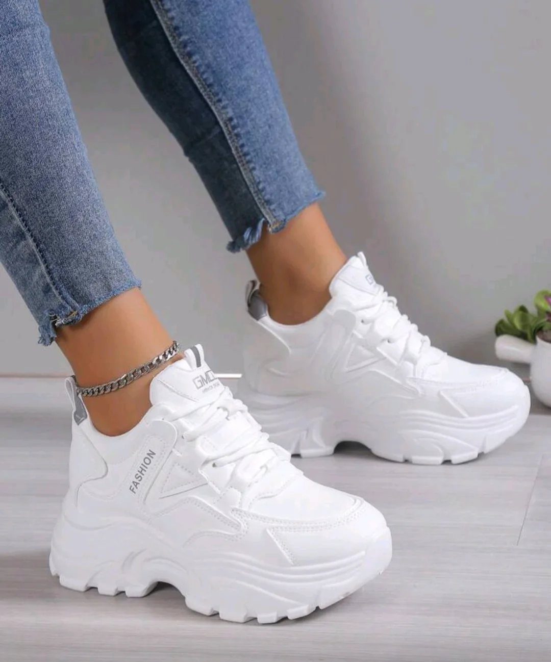 White chunky platform sneakers worn by a person in blue denim jeans.