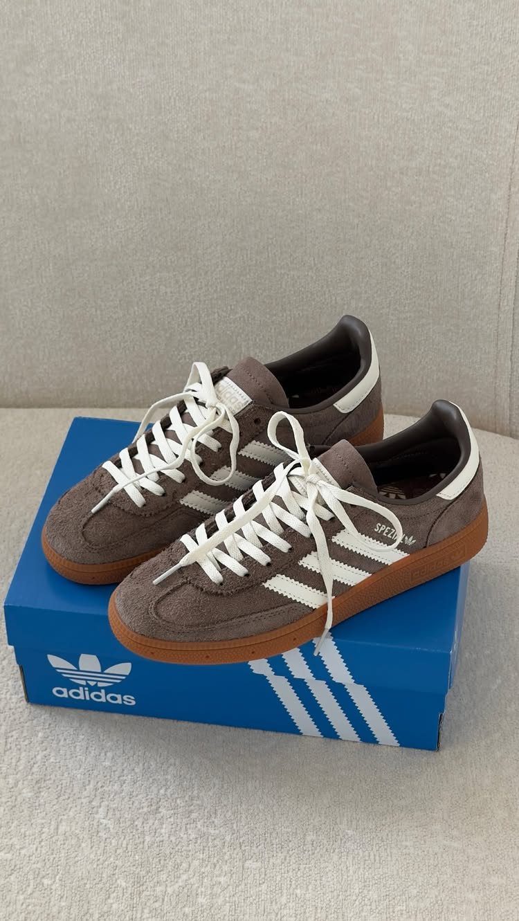 Brown suede Adidas sneakers with white stripes and laces sitting on a blue shoebox.