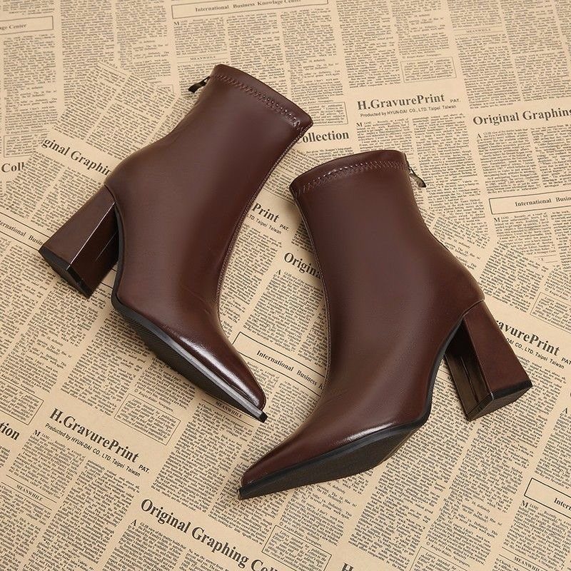 Brown leather ankle boots with pointed toes and block heels on a newspaper print background.