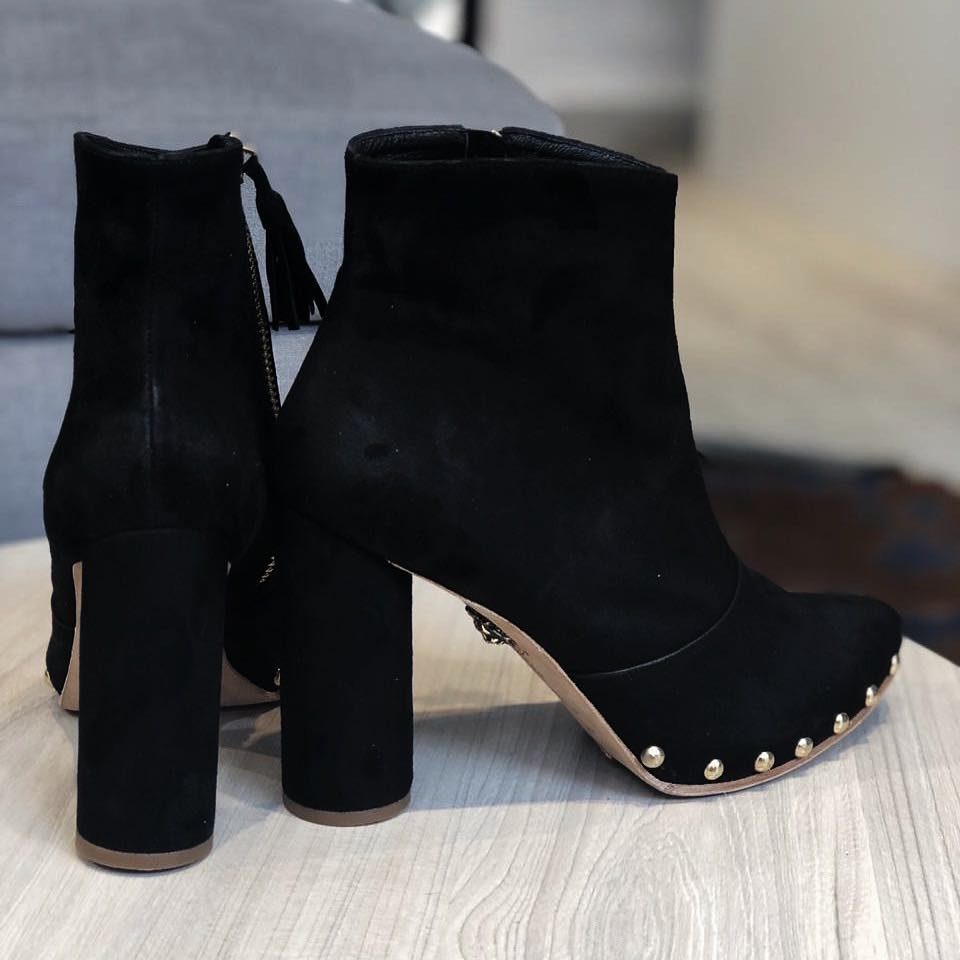 Black suede ankle boots with gold studs and thick block heels on a wooden surface.