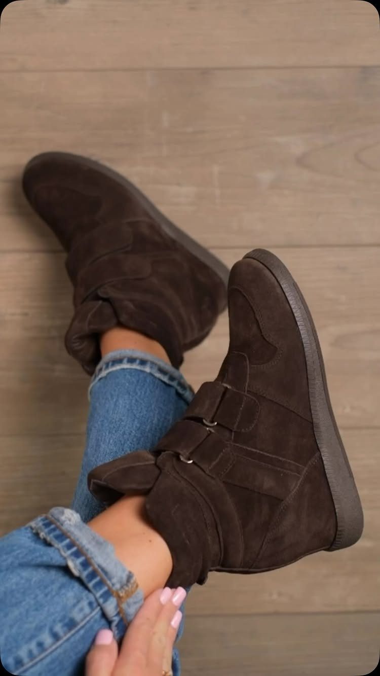 Brown suede high-top boots worn with blue denim jeans on a wooden floor.