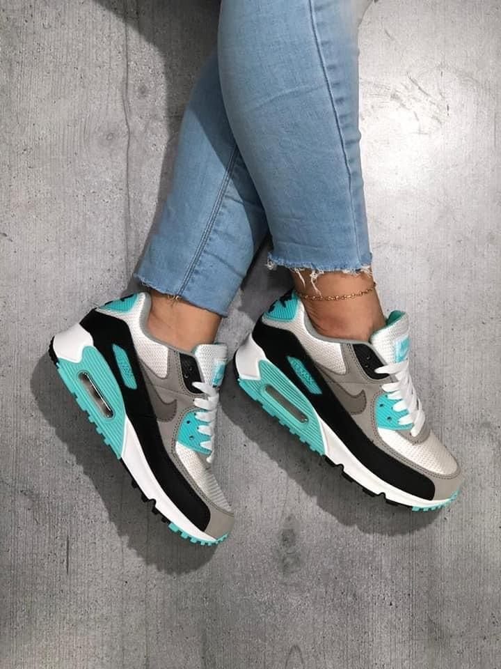 Person wearing light blue jeans and grey, black, and turquoise sneakers on concrete.