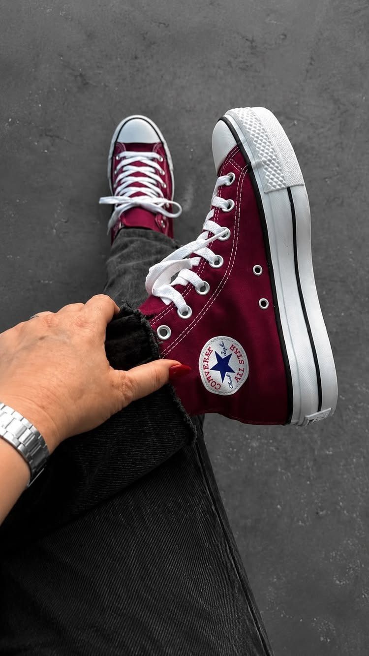 Maroon high-top Converse sneakers worn with dark grey denim jeans on grey pavement.