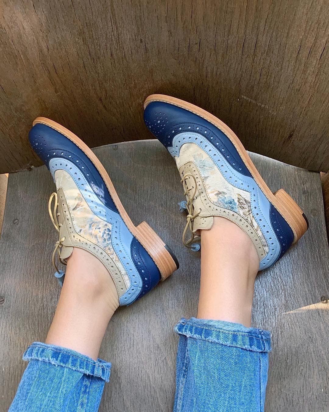 Person wearing blue and tan patterned brogue shoes with cuffed blue denim jeans.