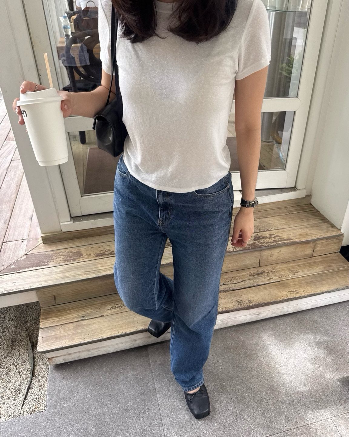 Person in white t-shirt and blue jeans wearing black ballet flats on wooden steps.