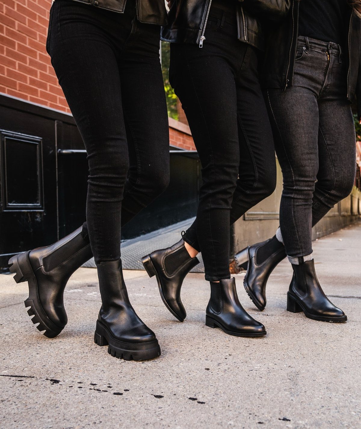 Three people walking on a sidewalk wearing black skinny jeans and various black leather boots.