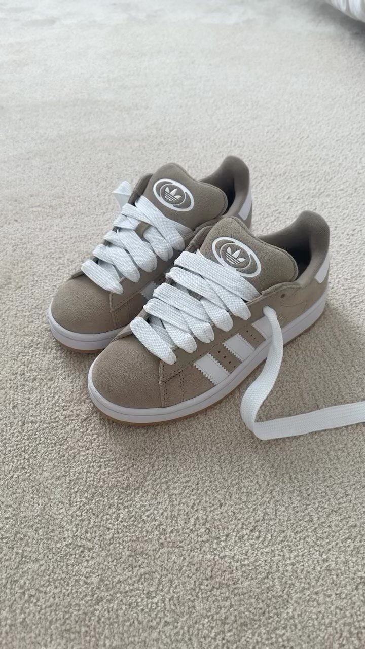 Tan suede Adidas sneakers with white laces sitting on a light beige carpeted floor.