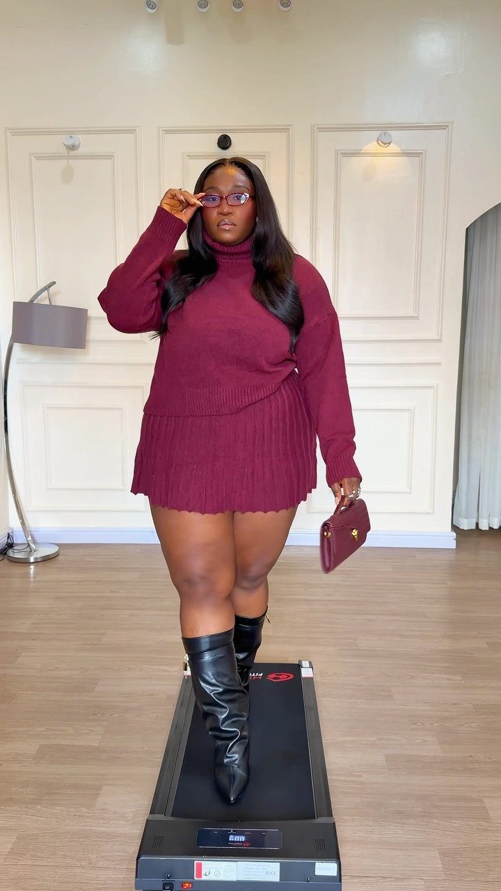 Woman in a burgundy sweater dress and black knee-high boots standing on a treadmill.