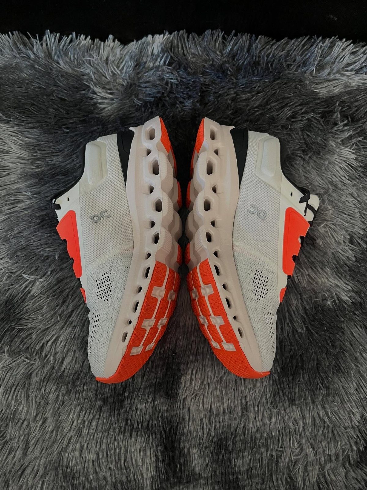White and orange athletic running shoes resting on a grey textured faux fur rug.