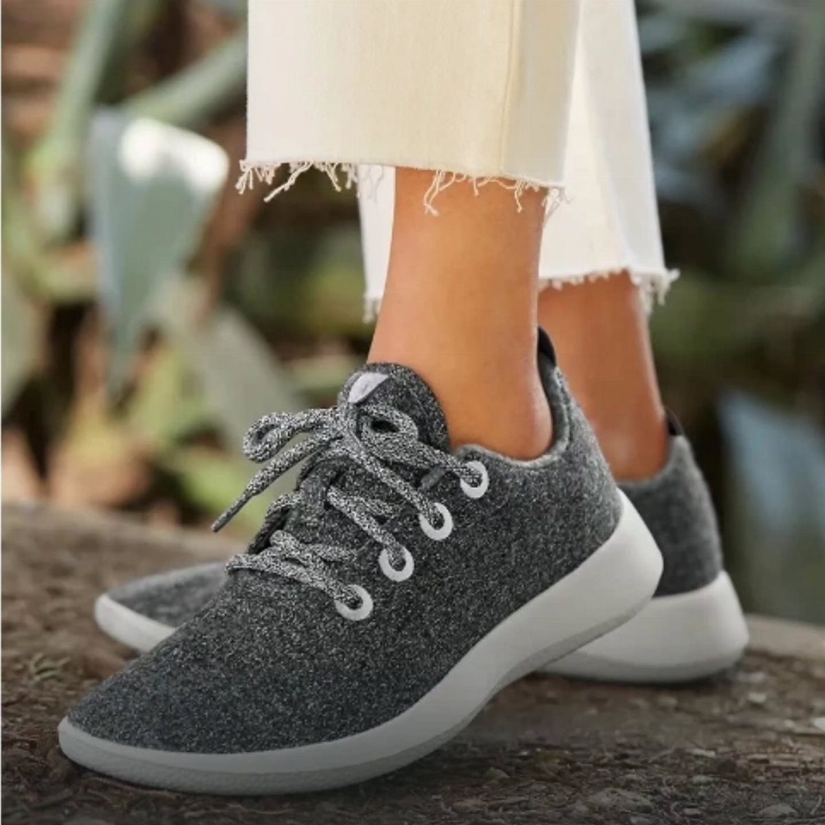 Grey wool sneakers with white soles worn by a person in white denim jeans.