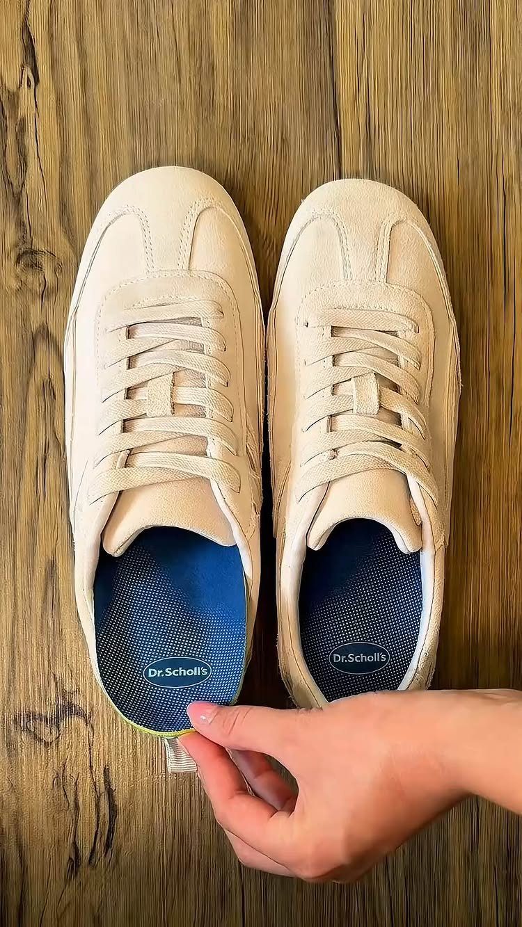 Beige suede sneakers on a wooden floor with one insole lifted to show the brand name.