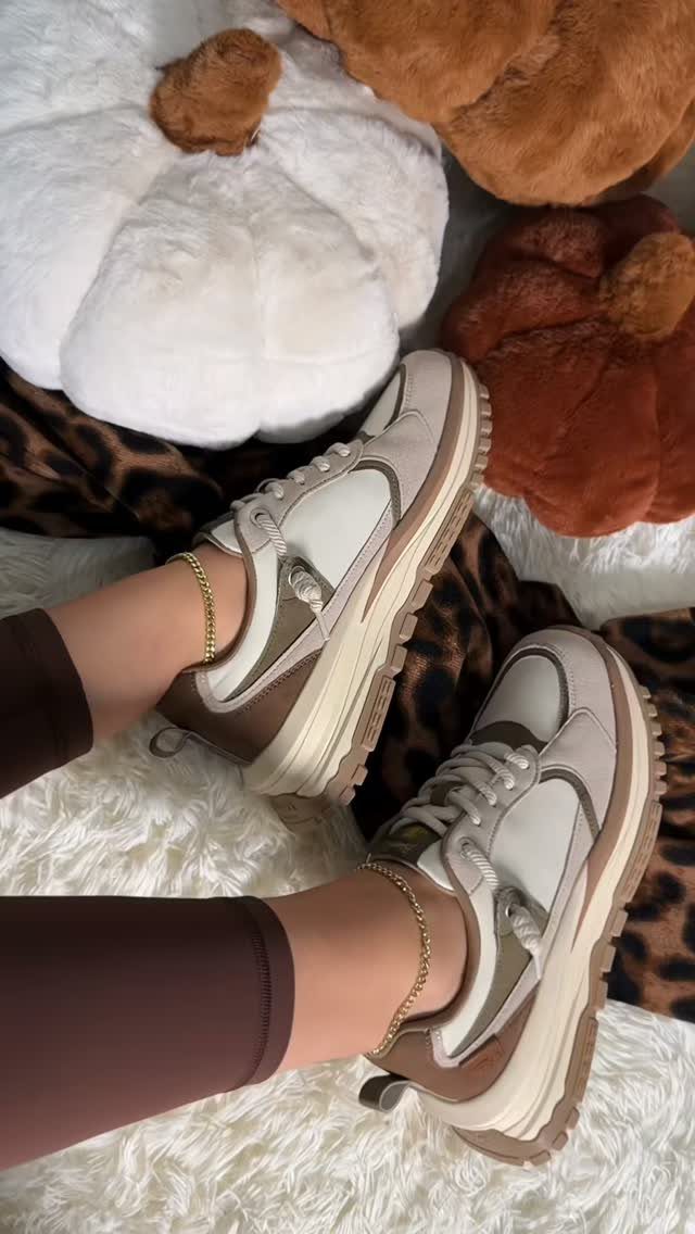 Person wearing white and brown platform sneakers and gold anklets on white faux fur.