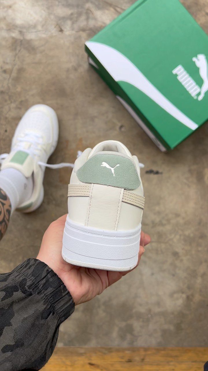 A hand holding a cream Puma sneaker with a light green accent near its box.