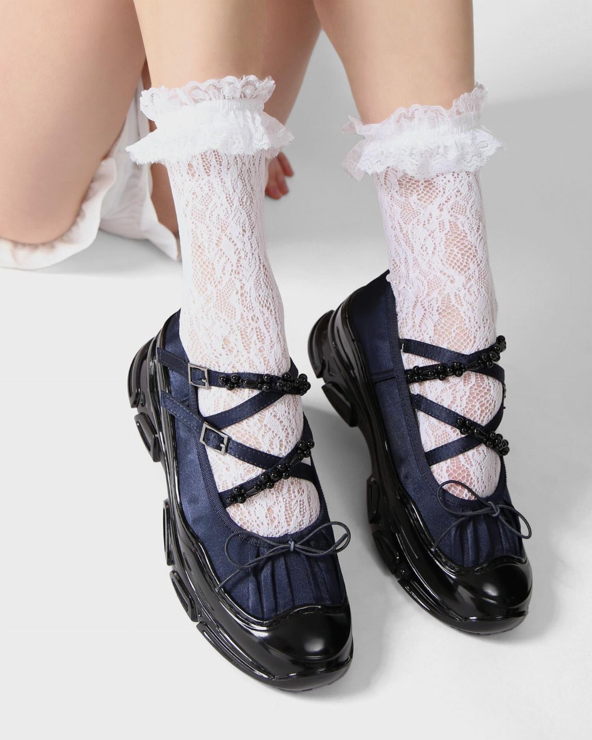 Navy blue ballet sneakers with crisscross straps worn with white lace ruffled socks.