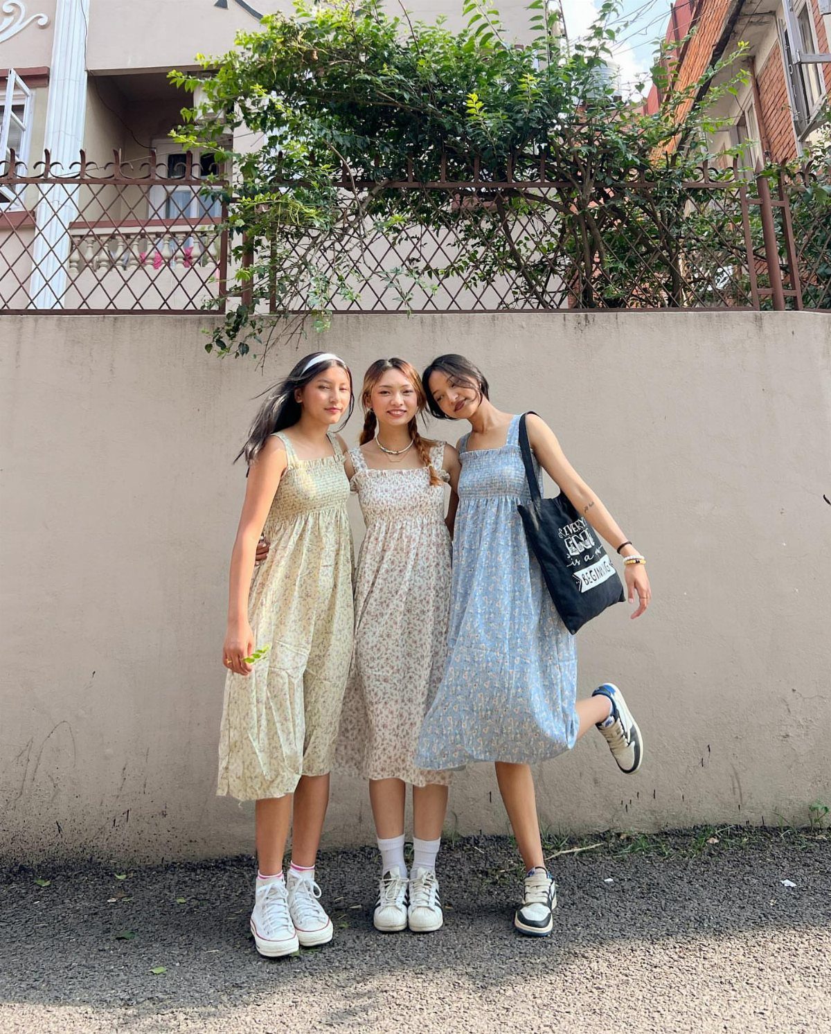 Three women posing in patterned midi dresses and white sneakers against a wall.